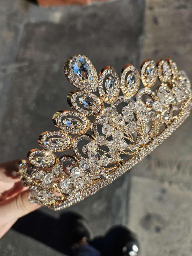 May include: A gold crown with clear rhinestones. The crown is made of metal and has a delicate design.