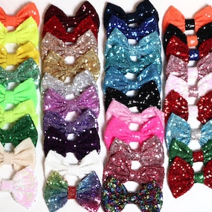 May include: A collection of 20 colorful sequined bows in various colors, including pink, blue, green, red, yellow, and white. The bows are arranged in rows and are all made of the same material.