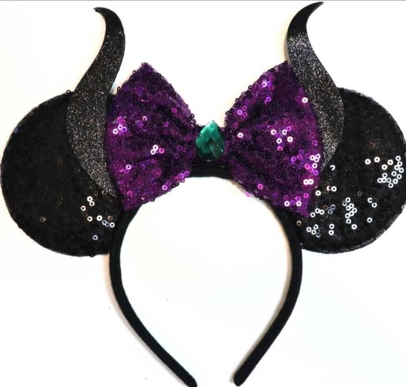 May include: Black headband with large black ears covered in sequins and a purple sequined bow with a green gem in the center.