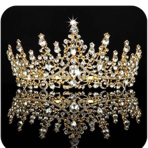 Pode incluir: Uma coroa dourada com numerosos cristais claros e brilhantes. A coroa tem um design ornamentado e sim&eacute;trico, com uma superf&iacute;cie refletora por baixo, sobre um fundo preto.