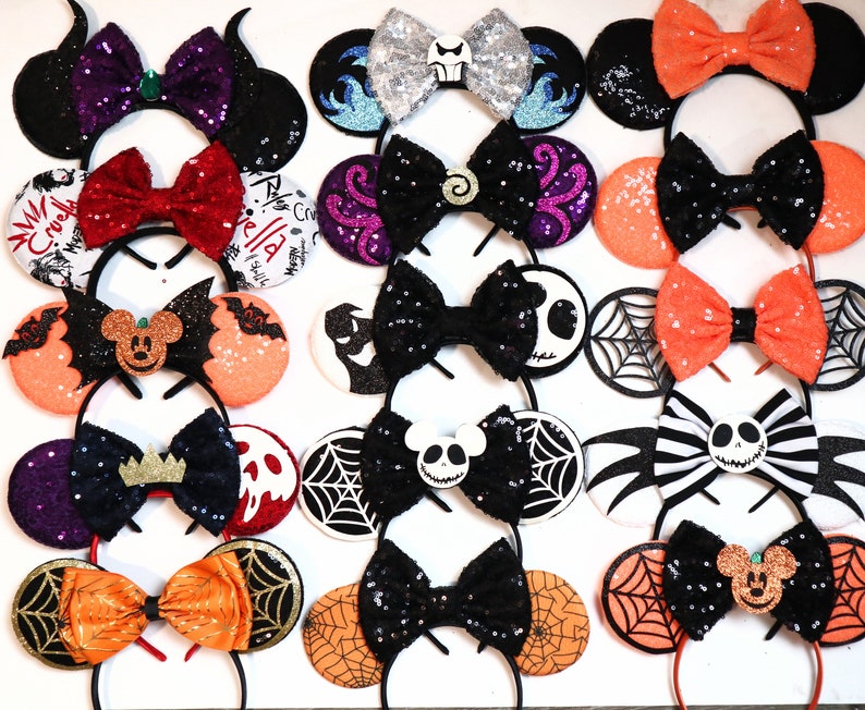 May include: A collection of 15 pairs of handmade Disney-themed mouse ears with various characters and designs. The ears are made with glitter fabric and feature bows, ribbons, and other embellishments. Some of the characters featured include Mickey Mouse, Minnie Mouse, Jack Skellington, and Ursula.