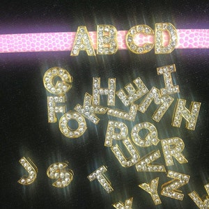 May include: Gold-toned alphabet letter charms with clear rhinestones. The letters A, B, C, D, F, G, H, I, J, K, L, M, N, O, P, Q, R, S, T, U, V, W, X, Y, and Z are visible.