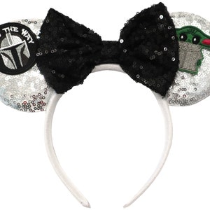 May include: Silver sequin Minnie Mouse ears headband with a black bow, a green character patch, and a black and white patch that says "This is the way".