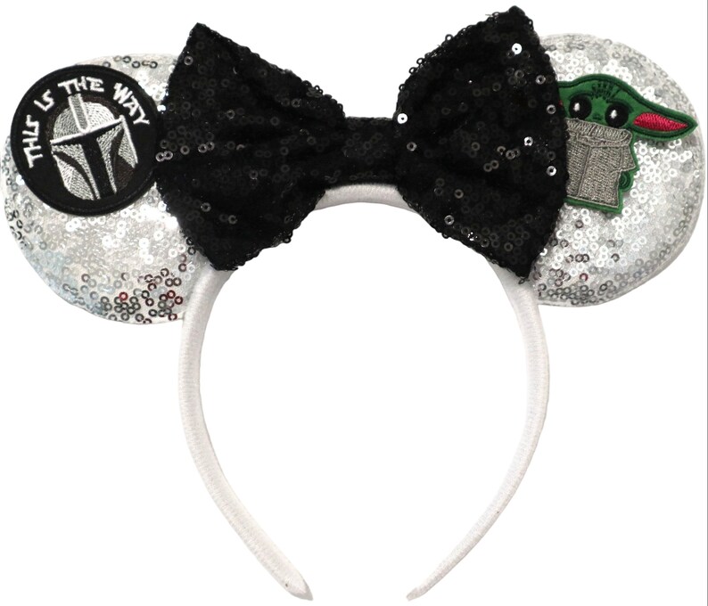May include: Silver sequin Minnie Mouse ears headband with a black bow, a green character patch, and a black and white patch that says "This is the way".