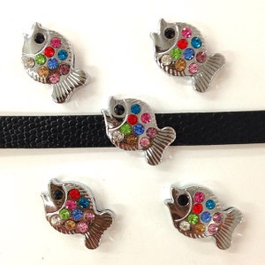 May include: Five silver fish charms with colorful rhinestones. Each charm features a silver fish shape with a black rhinestone for an eye and a variety of colorful rhinestones covering the body.