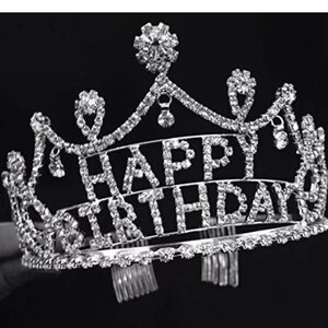 Pode incluir: Tiara prateada com as palavras "HAPPY BIRTHDAY" em strass transparentes e brilhantes. A tiara tem um design decorativo e ornamentado com detalhes de cristal pendurados, perfeita para uma festa de anivers&aacute;rio.