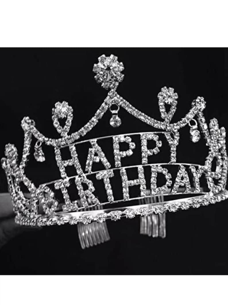 Pode incluir: Tiara prateada com as palavras "HAPPY BIRTHDAY" em strass transparentes e brilhantes. A tiara tem um design decorativo e ornamentado com detalhes de cristal pendurados, perfeita para uma festa de anivers&aacute;rio.