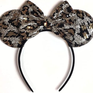 May include: Black headband with large, gold and silver sequined ears and a matching bow. The sequins are in a leopard print pattern.
