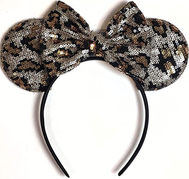 May include: Black headband with large, gold and silver sequined ears and a matching bow. The sequins are in a leopard print pattern.