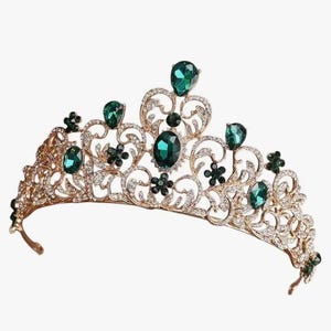 Pode incluir: Uma tiara dourada com pedras preciosas verde esmeralda e strass transparentes. A tiara apresenta um design ornamental de filigrana com pedras verdes ovais e em forma de gota. Para uma ocasi&atilde;o especial.