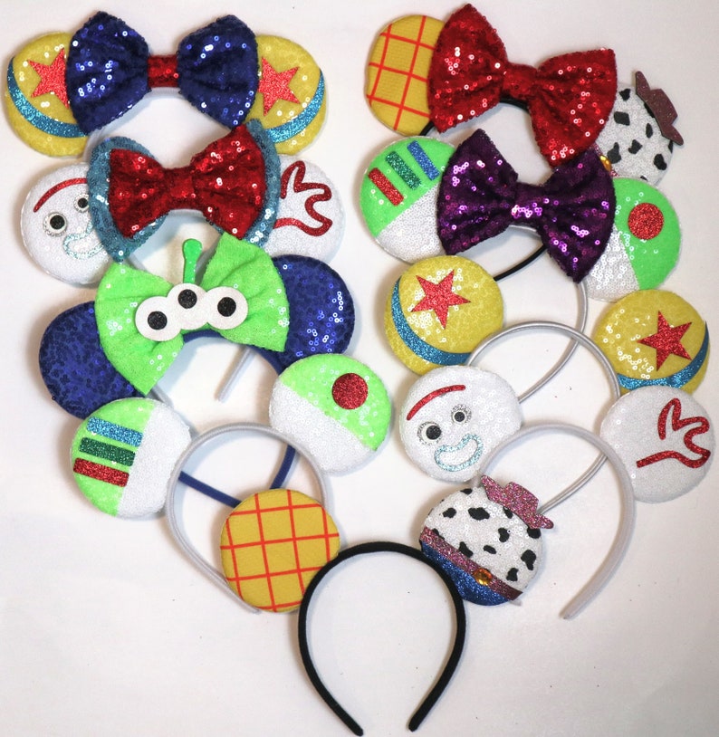 May include: A set of 10 Toy Story themed Disney-style character ears. The ears are made of felt and glitter and feature characters like Woody, Buzz Lightyear, and the aliens.