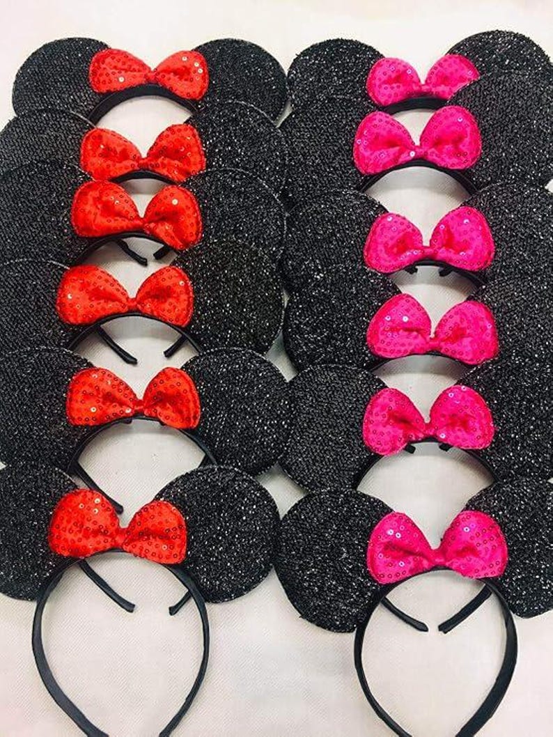 May include: Black sequined mouse ear headbands with red sequin bows and pink sequin bows. The ears are round and attached to a black headband. The bows are centered on the ears.