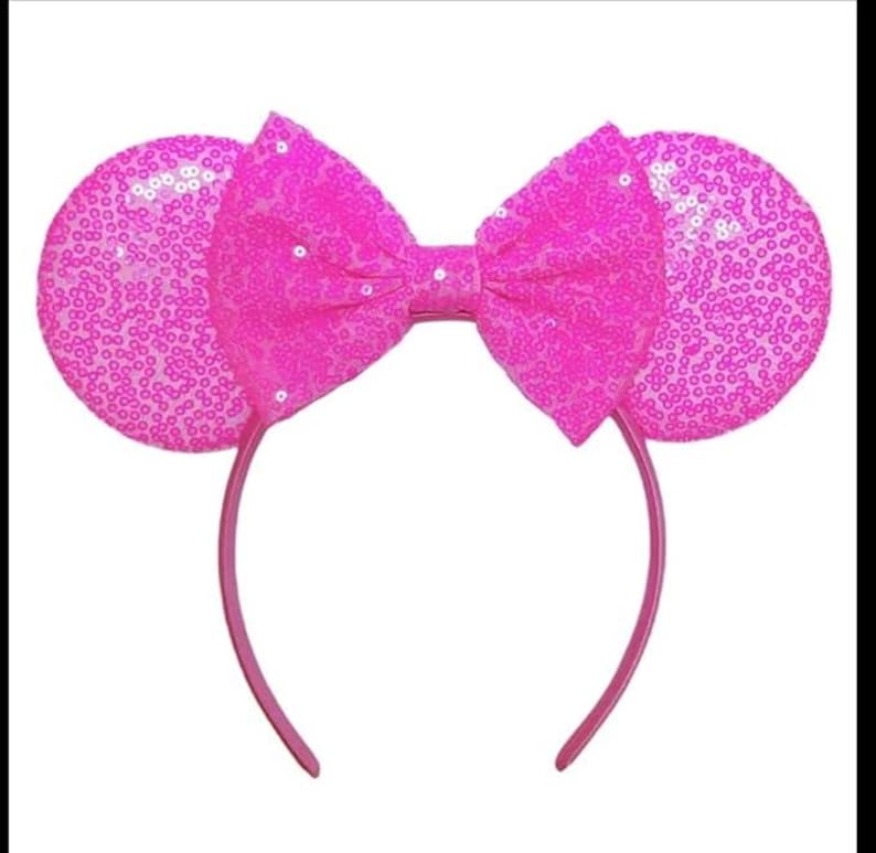 May include: A bright pink headband featuring two circular ears covered in shimmering sequins. A large, matching pink fabric bow with a sequined texture is positioned centrally between the ears, creating a cohesive and vibrant accessory design.