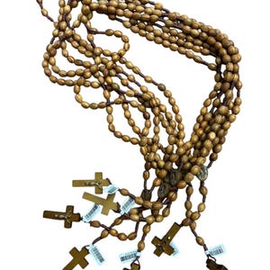 May include: Several rosaries with wooden beads and crosses. The beads are oval-shaped and light brown. The crosses are a darker brown and have a simple design. Each rosary has a tag attached.