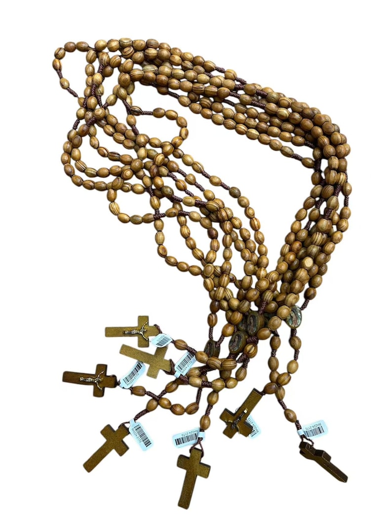 May include: Several rosaries with wooden beads and crosses. The beads are oval-shaped and light brown. The crosses are a darker brown and have a simple design. Each rosary has a tag attached.