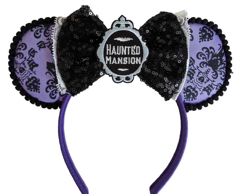 May include: Purple and black Haunted Mansion Mickey Mouse ears with a black bow and a silver charm that says "Haunted Mansion".