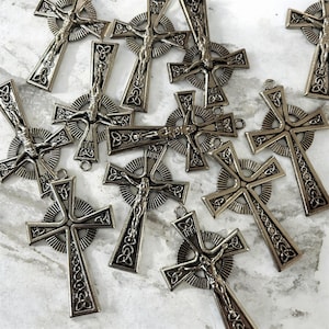 May include: A collection of silver-toned metal crucifix pendants featuring a central figure of Jesus, a circular halo design, and intricate Celtic knotwork patterns at the ends of the cross arms. Each pendant includes the letters INRI at the top.