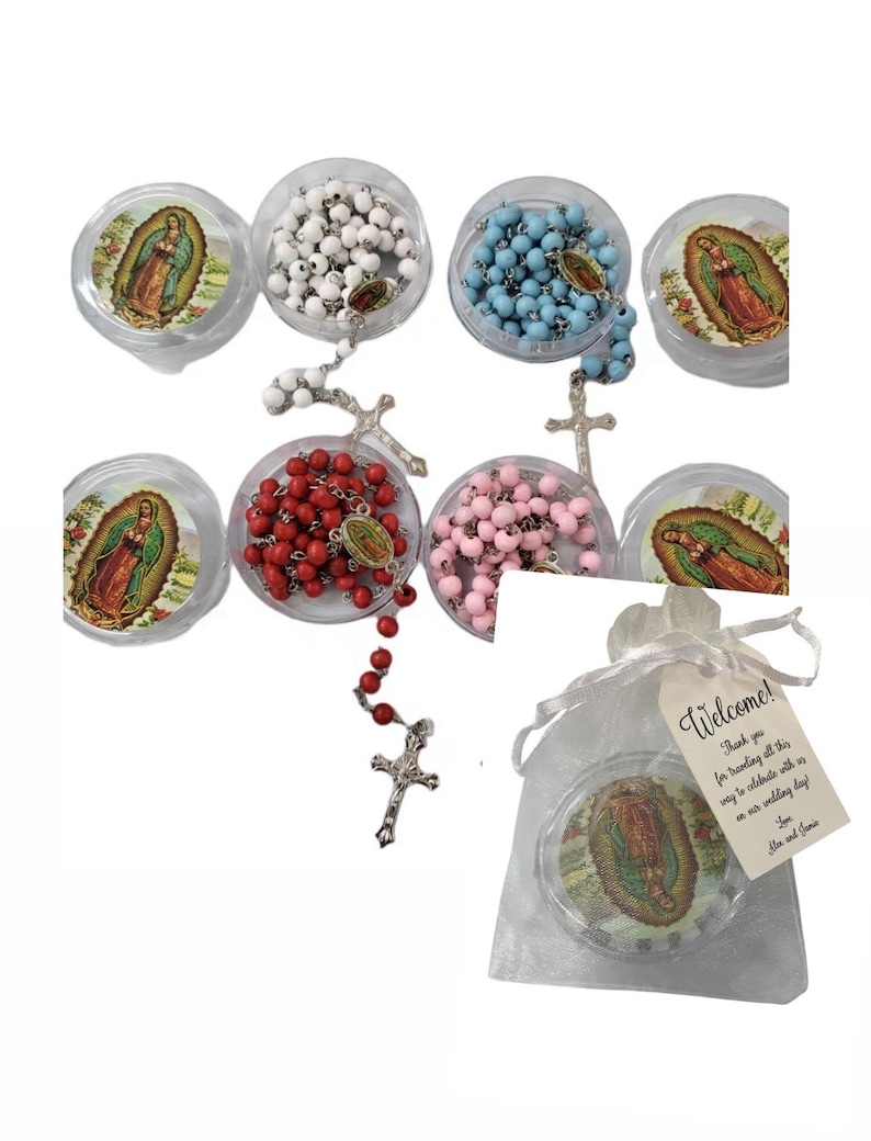 May include: Assortment of rosaries in clear plastic containers, featuring white, blue, red, and pink beads. Each rosary has a silver-tone cross. One rosary is displayed outside its container. A small gift bag with a tag that says "Welcome!" is also included.