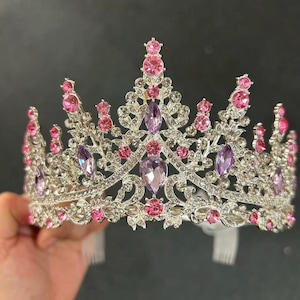Pode incluir: Uma coroa prateada com pedras preciosas rosa e roxas. A coroa apresenta um design de filigrana detalhado e &eacute; adornada com pedras rosas e roxas de v&aacute;rios tamanhos, redondas e ovais. A coroa tem formato de tiara e &eacute; projetada para eventos formais.