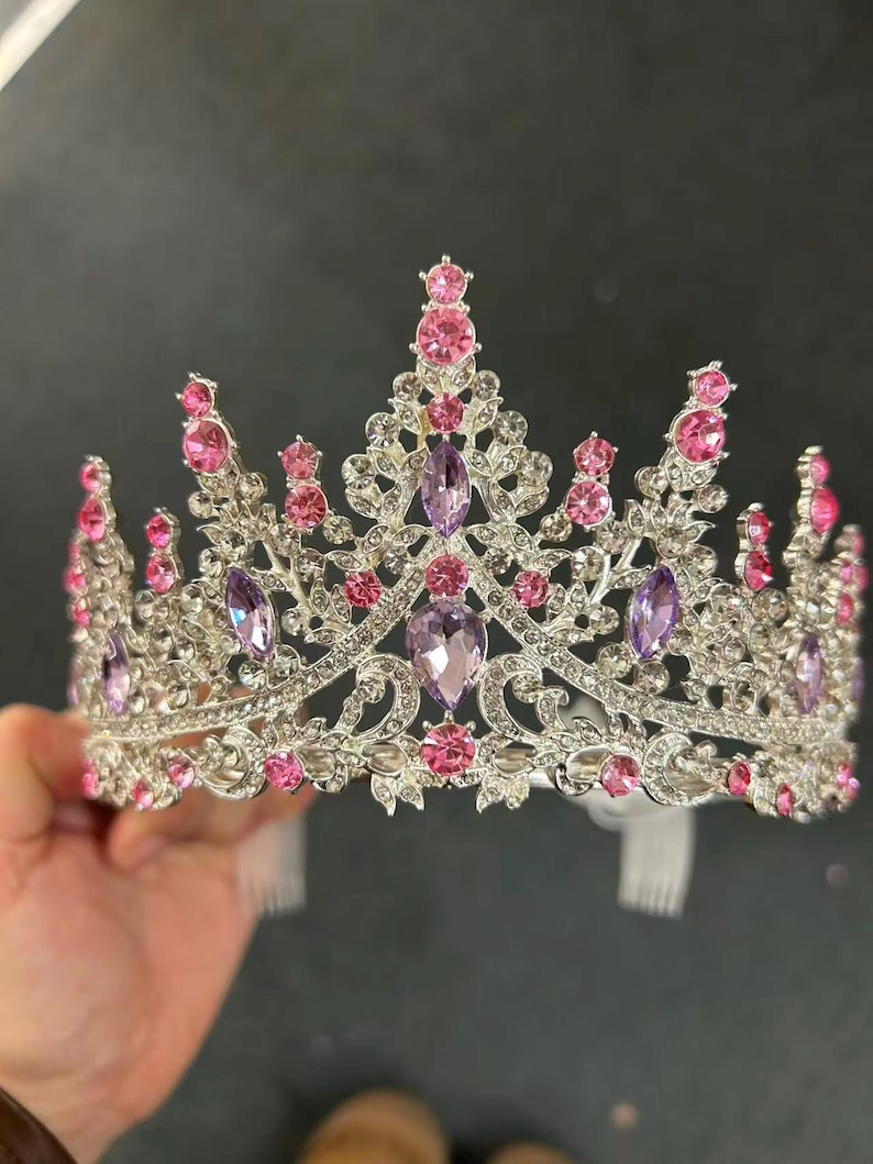 Pode incluir: Uma coroa prateada com pedras preciosas rosa e roxas. A coroa apresenta um design de filigrana detalhado e &eacute; adornada com pedras rosas e roxas de v&aacute;rios tamanhos, redondas e ovais. A coroa tem formato de tiara e &eacute; projetada para eventos formais.