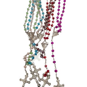 May include: A collection of rosaries in various colors, including blue, green, red, and purple. Each rosary features a crucifix and a series of beads. The beads are made of a shiny, possibly crystal-like material.
