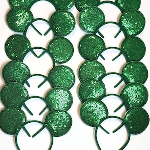 May include: A collection of green sequined mouse ear headbands. The ears are round and covered in shimmering green sequins. The headbands are a matching green color. The items are arranged in rows and columns on a white background.