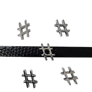 May include: Five silver metal charms shaped like the hashtag symbol. The charms are arranged in a pattern on a black leather background.