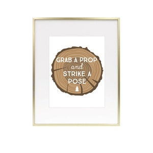 May include: A gold-framed print with a woodgrain background and the text "Grab a prop and strike a pose".