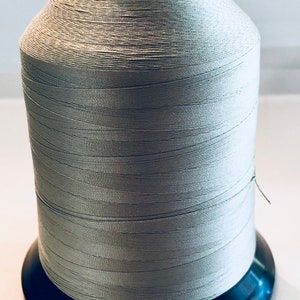 May include: A spool of light gray thread wound on a black plastic bobbin.