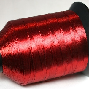 May include: A spool of red metallic thread wound on a black plastic bobbin.