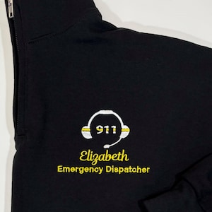 May include: Black 1/4 zip sweatshirt with a white embroidered headset with the text "911" and the text "Elizabeth Emergency Dispatcher" in yellow.