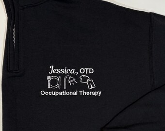 May include: Black long-sleeve sweatshirt with a white zipper and a white embroidered design that says "Jessica, OTD" and "Occupational Therapy" with icons of a fork, shower, shirt, and pants.