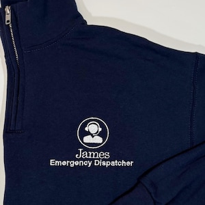 May include: A dark blue 1/4 zip sweatshirt with a white embroidered logo of a person with a headset and the text "James Emergency Dispatcher".