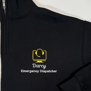 May include: Black mock neck sweatshirt with a yellow embroidered logo of a computer monitor with a headset and the text "Darcy Emergency Dispatcher".