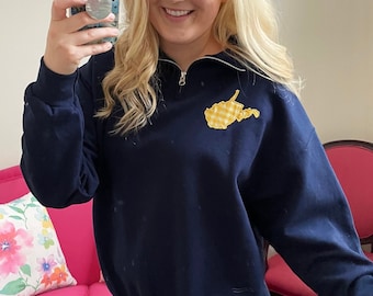 May include: A navy blue sweatshirt with a yellow and white checked West Virginia state outline on the front. The sweatshirt has a zip at the neck.