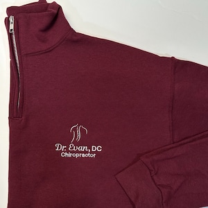 May include: Burgundy quarter-zip sweatshirt with a white embroidered logo that says "Dr. Evan, DC Chiropractor" and a stylized image of a spine.