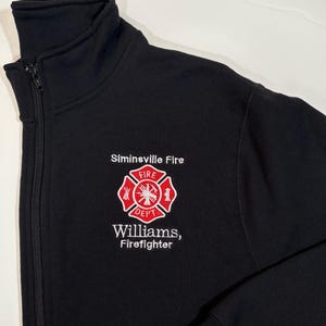 May include: Black zip-up jacket with a white embroidered fire department logo and the text "Siminsville Fire" and "Williams, Firefighter".