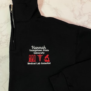 May include: Black zippered sweatshirt with a red embroidered design. The design includes the text "Hannah Youngstown State University Medical Lab Scientist" and three red icons: a test tube, a caduceus, and a microscope.