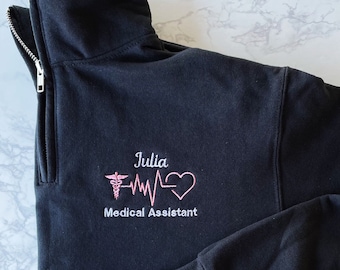 May include: Black fleece pullover with a zipper and a pink embroidered design that says "Julia Medical Assistant" with a caduceus and a heart beat.