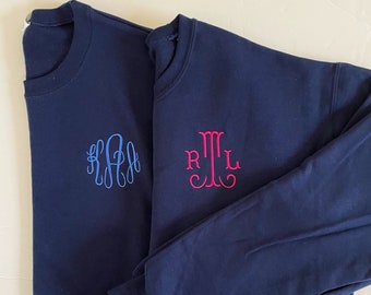 May include: Two navy blue long-sleeve shirts with embroidered monograms. One shirt has a light blue monogram, and the other has a pink monogram. The shirts are made of a soft, comfortable material.