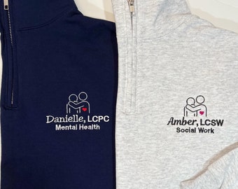 May include: Two gray and navy blue quarter-zip sweatshirts with embroidered logos. The gray sweatshirt has the text "Amber, LCSW Social Work" and the navy blue sweatshirt has the text "Danielle, LCPC Mental Health".