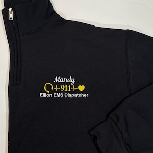 May include: Black sweatshirt with a white embroidered design that says "Mandy Q-911- Ellion EMS Dispatcher" with a yellow heart and a yellow headset.