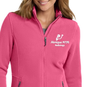 May include: A vibrant pink fleece jacket with a full zipper closure and two side pockets. The jacket features the text "Monique RT(R) Radiology" in white on the upper left chest. The jacket is a solid color and has a high collar.