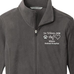 May include: Charcoal gray fleece jacket with a full zipper and two side pockets. The jacket features the text "Dr Wilson, DVM" above a paw print, heartbeat, and heart graphic, with "Wilson Animal Hospital" below.