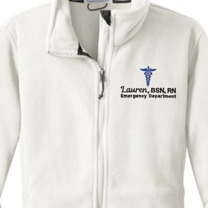 May include: White fleece jacket with a full zipper and a high collar. The jacket features a blue medical symbol and the text "Lauren, BSN, RN Emergency Department" on the upper left chest.