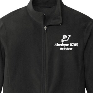 May include: Black fleece jacket with a full zipper, two side pockets, and a high collar. The jacket features the text "Monique RT(R) Radiology" and a small graphic of a skeleton in white on the upper left chest.