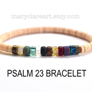 Puede incluir: Una pulsera de cuentas beige con cuentas de acento coloridas. La pulsera presenta una variedad de cuentas en colores como verde, azul, negro, marrón y dorado. El texto "PSALM 23 BRACELET" se muestra debajo.