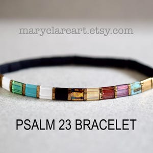 May include: A colorful bracelet with a black band and rectangular beads in various colors, including white, green, turquoise, black, and gold. The text "PSALM 23 BRACELET" is displayed below the bracelet.