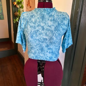 May include: A blue and white tie-dye crop top with a mock neck and short, flared sleeves. The top is on a dress form.
