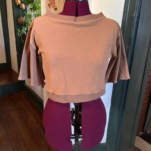May include: A brown waffle knit cropped top with a boat neck and 3/4 sleeves. The top is on a dress form.